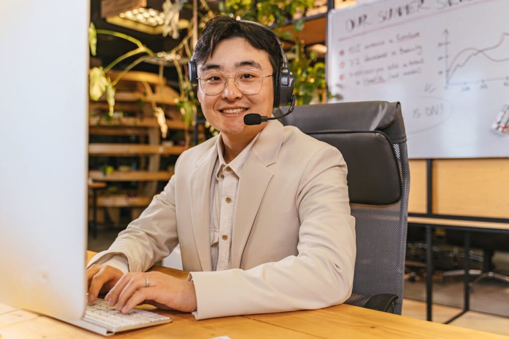 Smiling man with headphones in a stylish office environment, working on a computer.